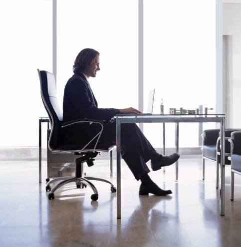 Businessman wearing dark suit sitting indoors in an office at a desk.